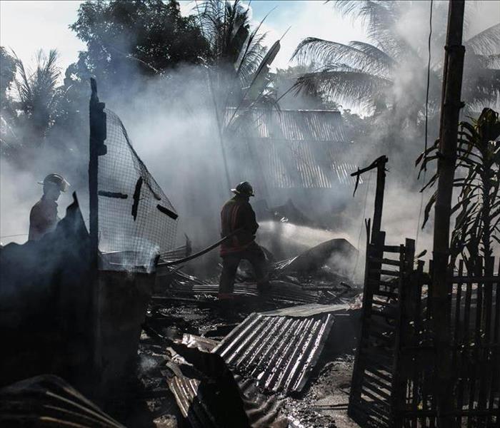 A firefighter sprays water on the charred remains of a house, surrounded by smoke and debris, after a house fire. 